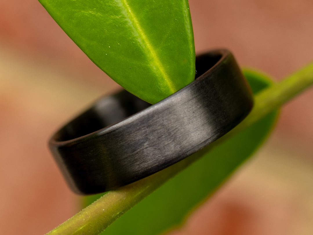 6mm uni-directional carbon fiber ring with matte finish, styled on a green plant stem for a natural outdoor aesthetic