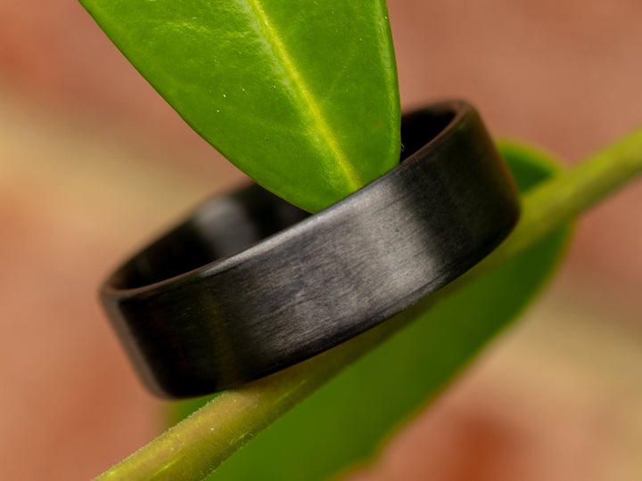 6mm uni-directional carbon fiber ring with matte finish, styled on a green plant stem for a natural outdoor aesthetic