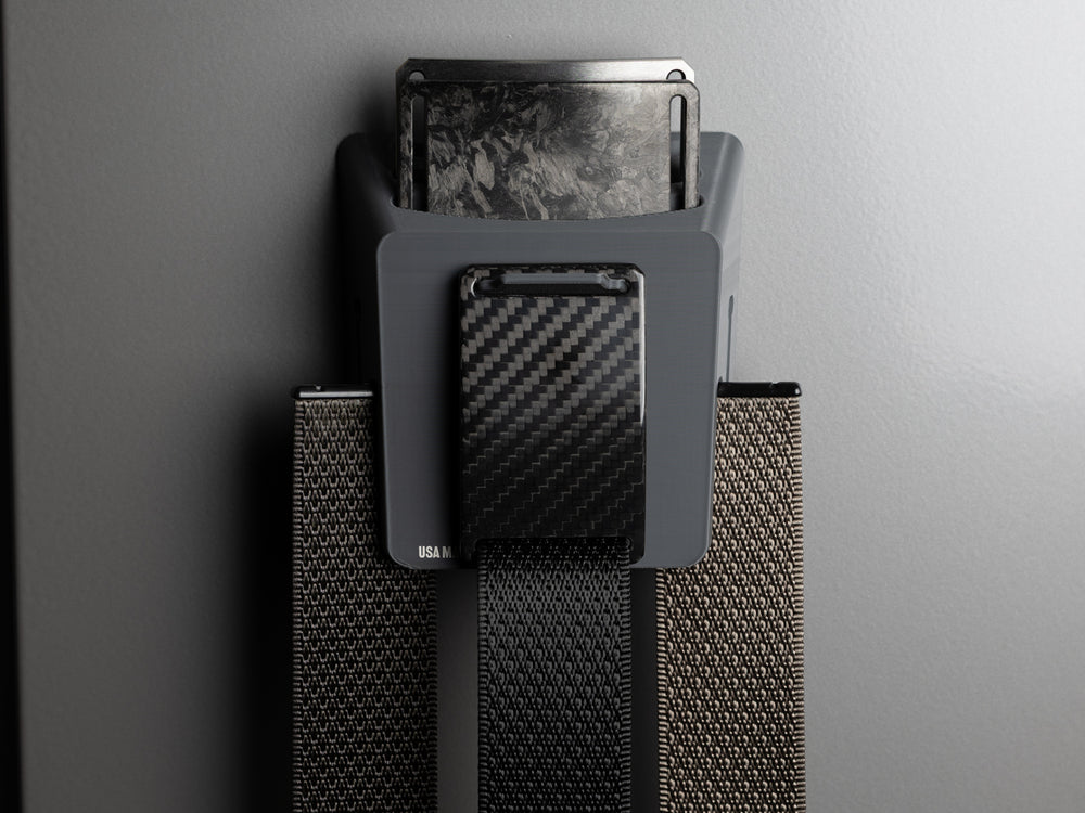 Mounted Grip6 Hub organizer displaying twill carbon fiber, forged carbon, and titanium belt buckles with matching straps.