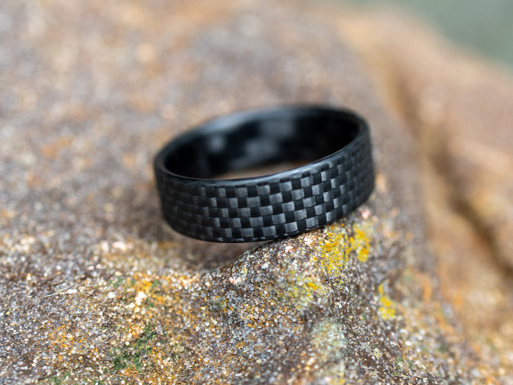 6mm carbon fiber Gridlock ring displayed on a rugged, textured rock surface, highlighting the detailed woven pattern.
