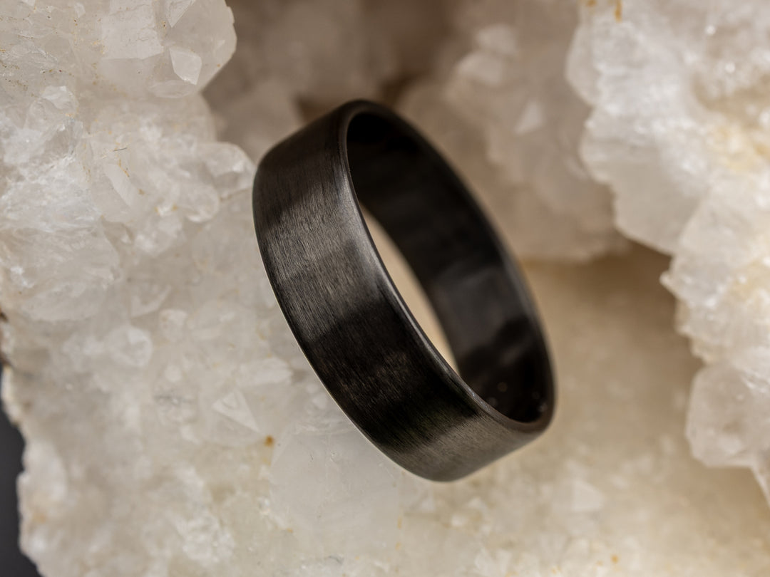6mm matte carbon fiber ring with uni-directional grain, resting in a white crystal geode for a natural contrast