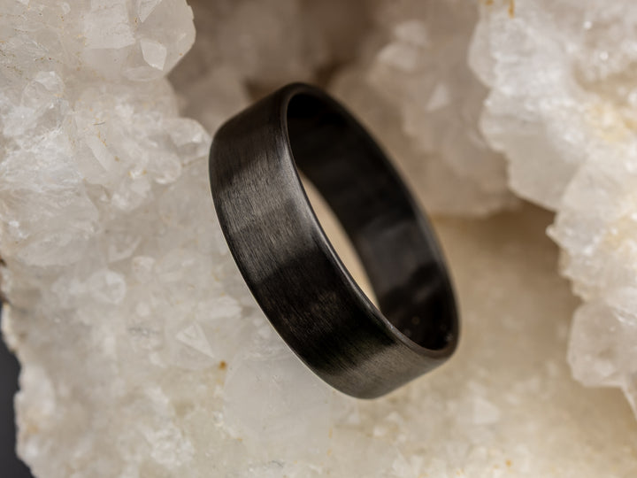 6mm matte carbon fiber ring with uni-directional grain, resting in a white crystal geode for a natural contrast