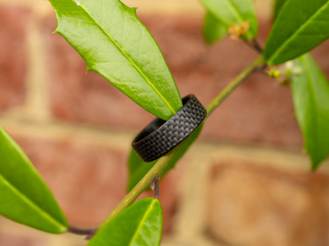 6mm carbon fiber Gridlock ring wrapped around a green leaf, contrasting nature with high-tech craftsmanship.
