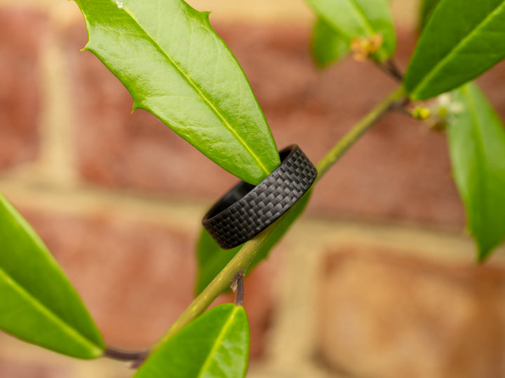 6mm carbon fiber Gridlock ring wrapped around a green leaf, contrasting nature with high-tech craftsmanship.