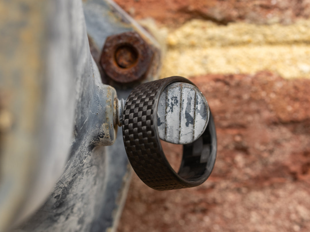 8mm Gridlock carbon fiber ring balanced on a weathered bolt, with an industrial backdrop showcasing its rugged durability and lightweight strength
