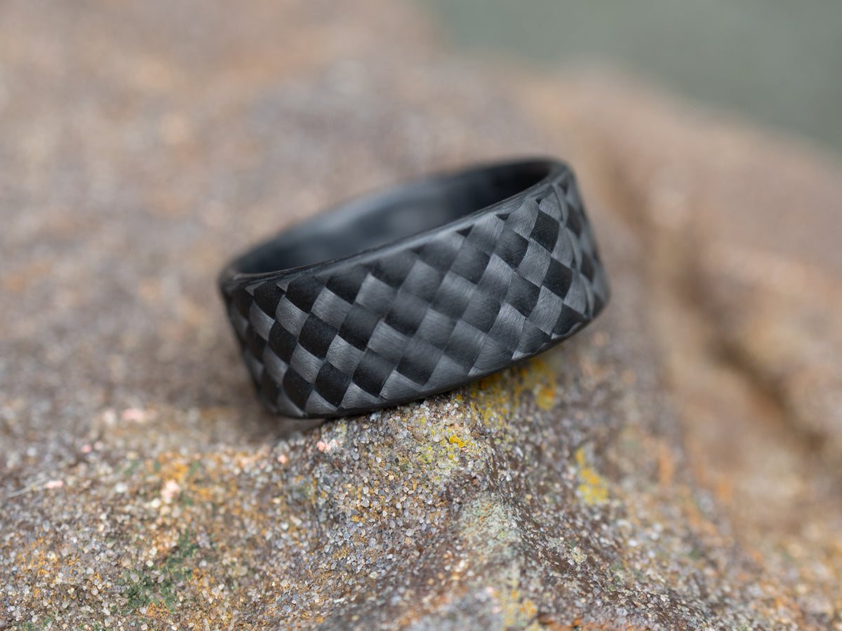 WeaveForce Vertex carbon fiber ring resting on a rock, emphasizing the ring’s sculpted texture and deep matte tone.