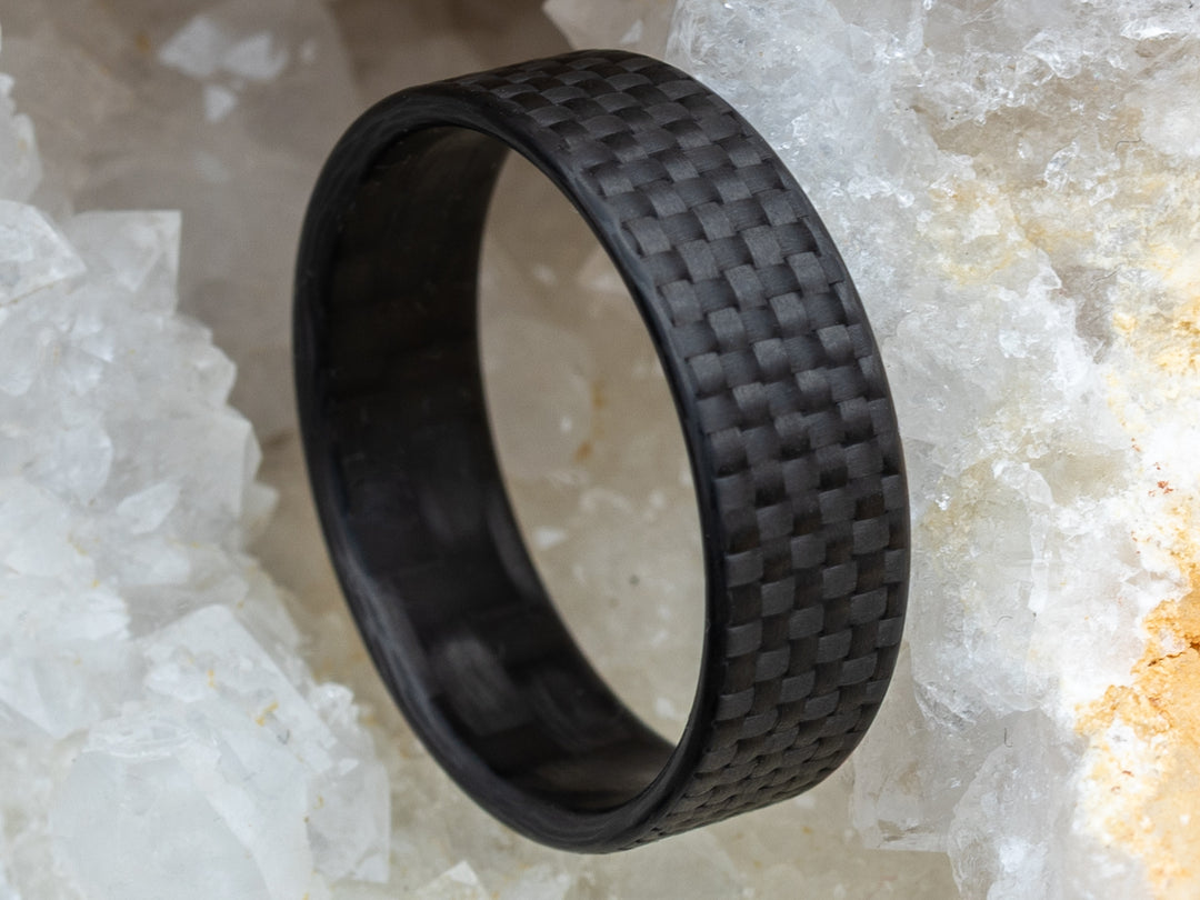 Close-up of the 6mm Gridlock carbon fiber ring nestled in a crystal geode, showcasing the ring’s checkered weave.