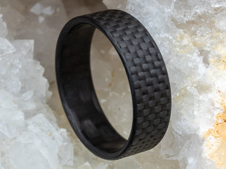 Close-up of the 6mm Gridlock carbon fiber ring nestled in a crystal geode, showcasing the ring’s checkered weave.