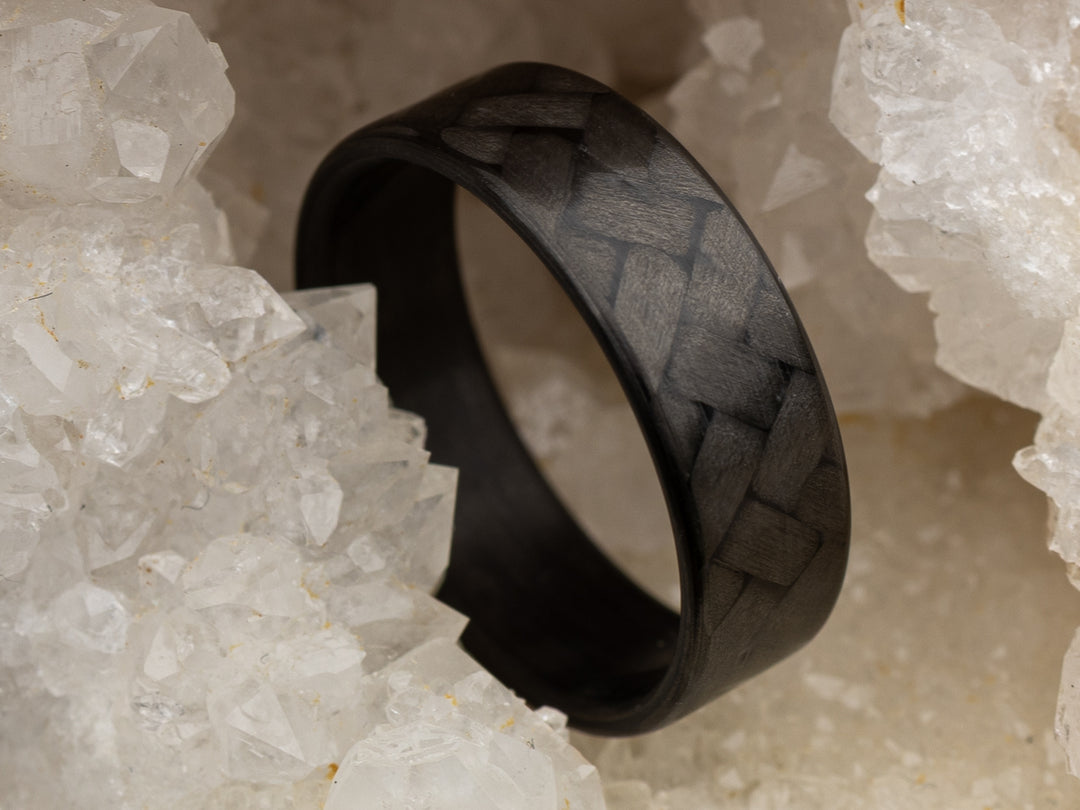 6mm carbon fiber ring with 45° twill weave pattern, resting in white crystal cluster for contrast and texture