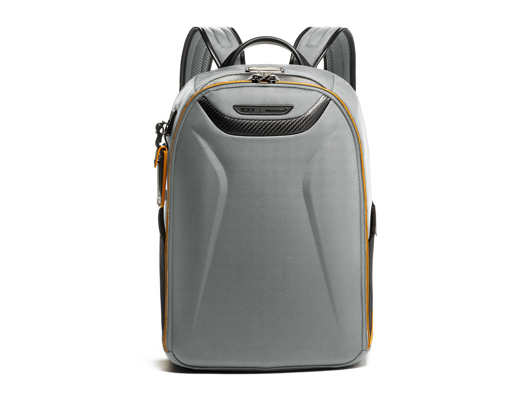 Close-up detail of TUMI McLaren Velocity backpack in grey showing carbon fiber panel and yellow accent zipper