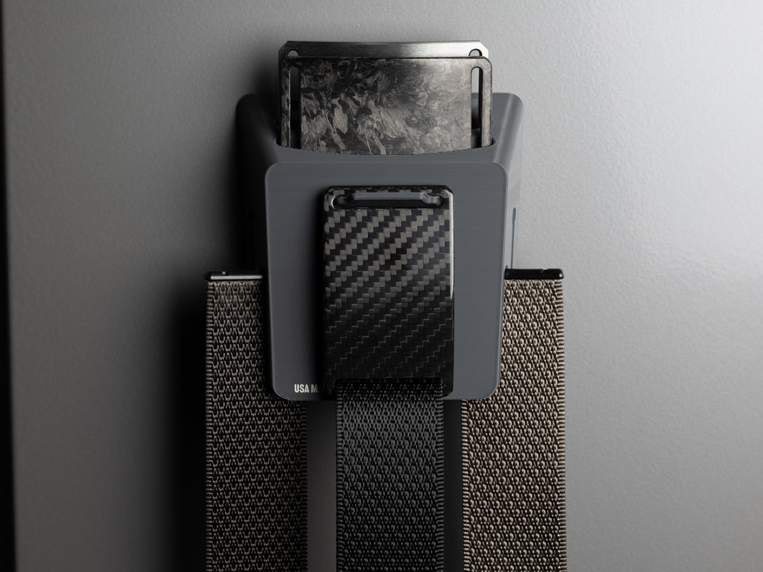 Mounted Grip6 Hub organizer displaying twill carbon fiber, forged carbon, and titanium belt buckles with matching straps.