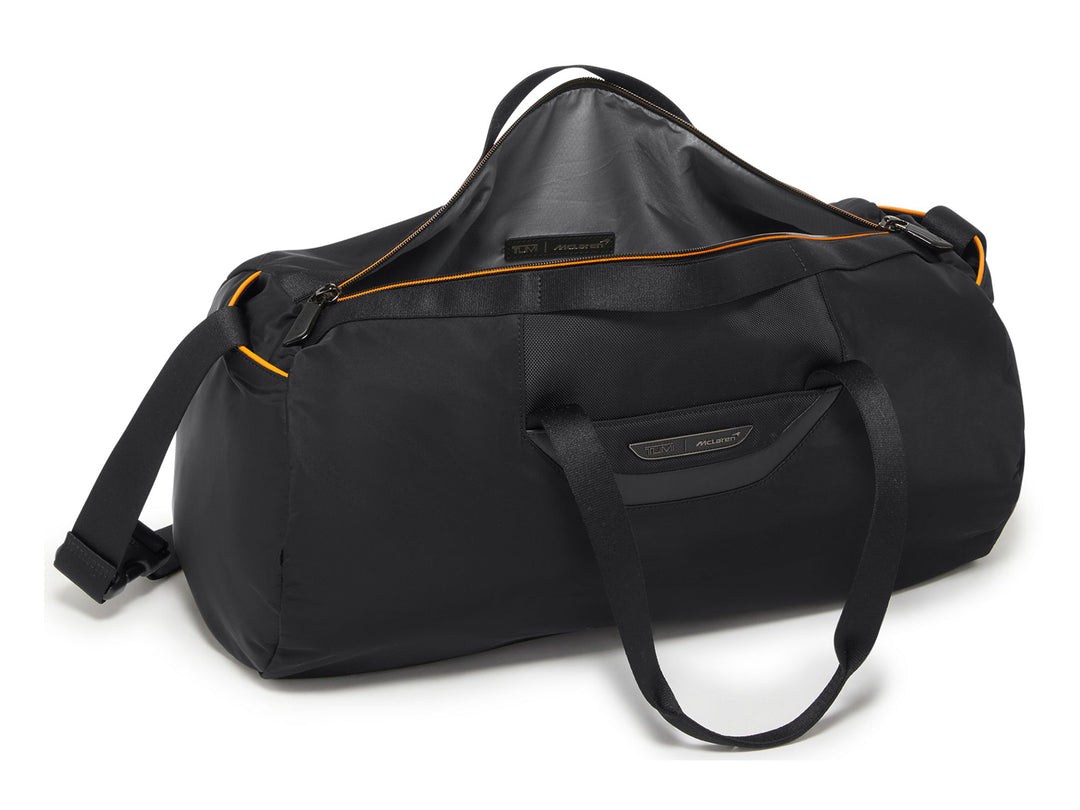 Side view of TUMI | McLaren Just In Case® Duffel in black with shoulder strap and orange trim.