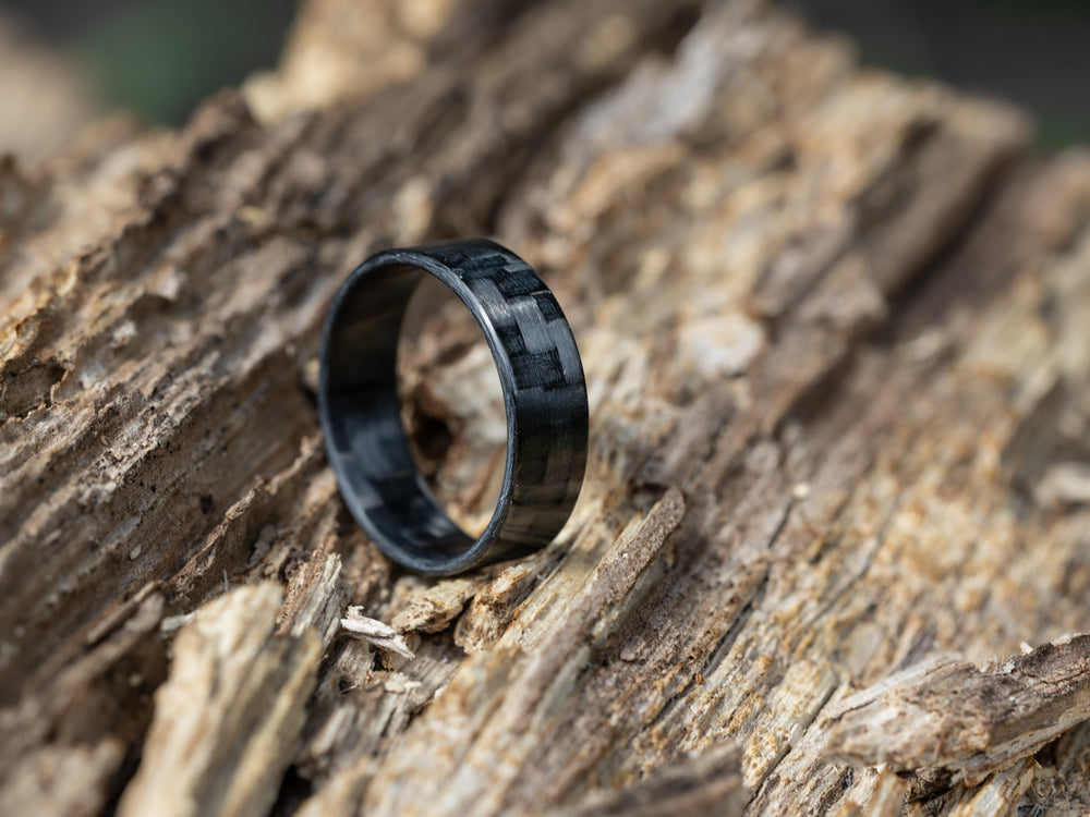 6mm carbon fiber ring with traditional twill weave, placed on textured tree bark in natural light