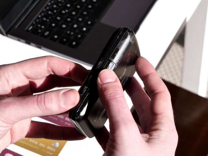Side view of a forged carbon fiber wallet being opened by hand, highlighting its snap-open clasp and slim, curved profile.