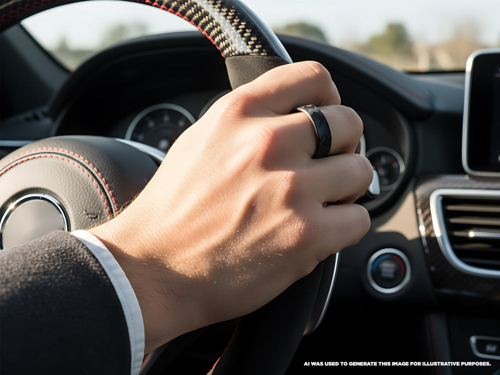Close-up of a hand wearing the Ultra Carbon Fiber Ring Forty-Five Narrow Polished while holding a car's steering wheel.
