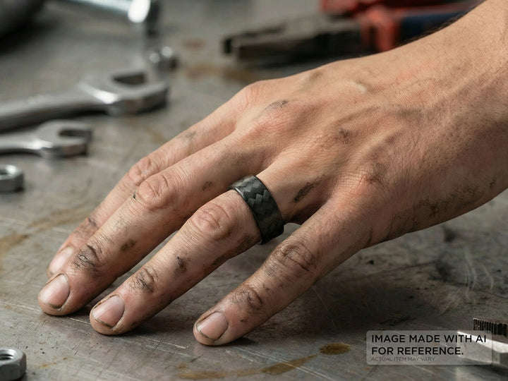 Hand wearing a carbon fiber ring on a workshop table with tools in the background