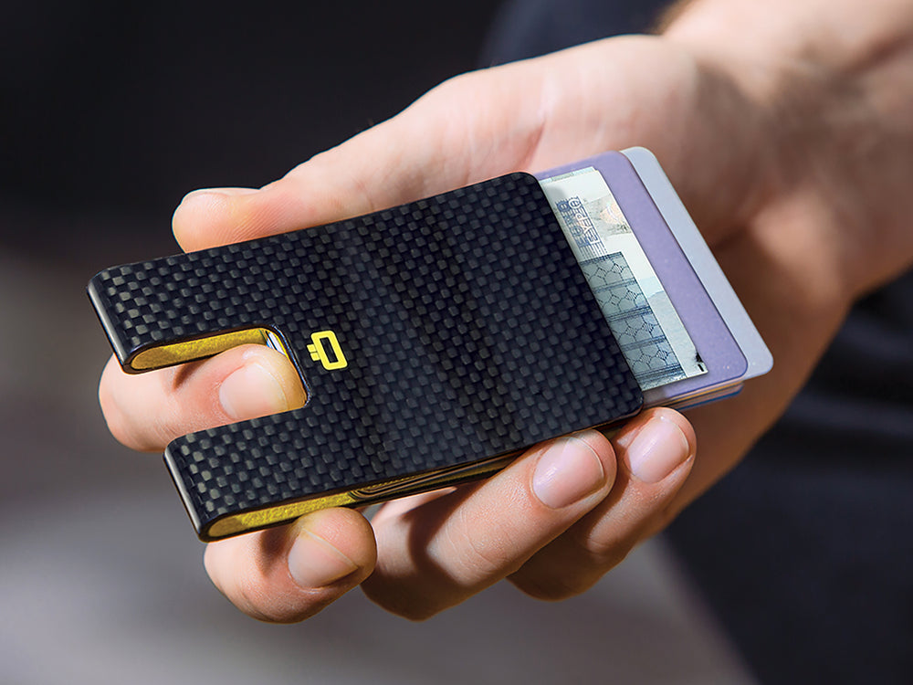 Person holding a carbon fiber card clip with cash and cards partially inserted, highlighting its functionality.