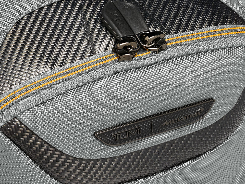 Macro detail shot of TUMI McLaren logo and carbon fiber weave pattern with yellow zipper accent