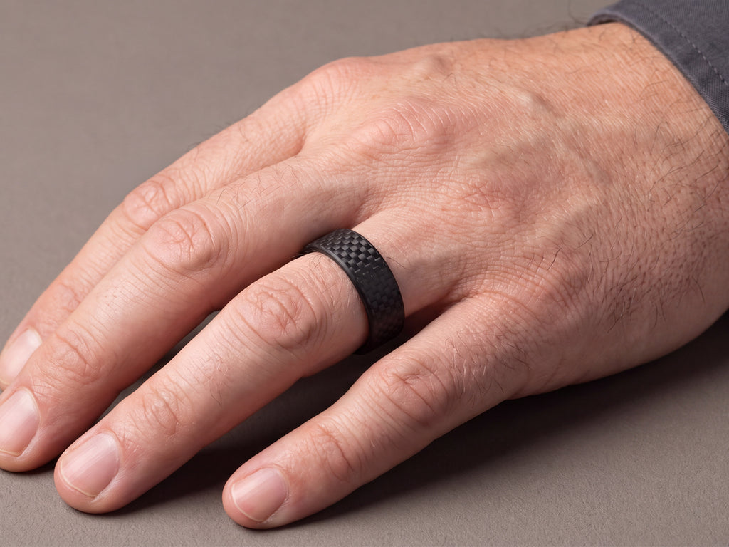 CarbonFG WeaveForce Gridlock 6mm carbon fiber ring worn on a left ring finger, hand at rest on a gray surface