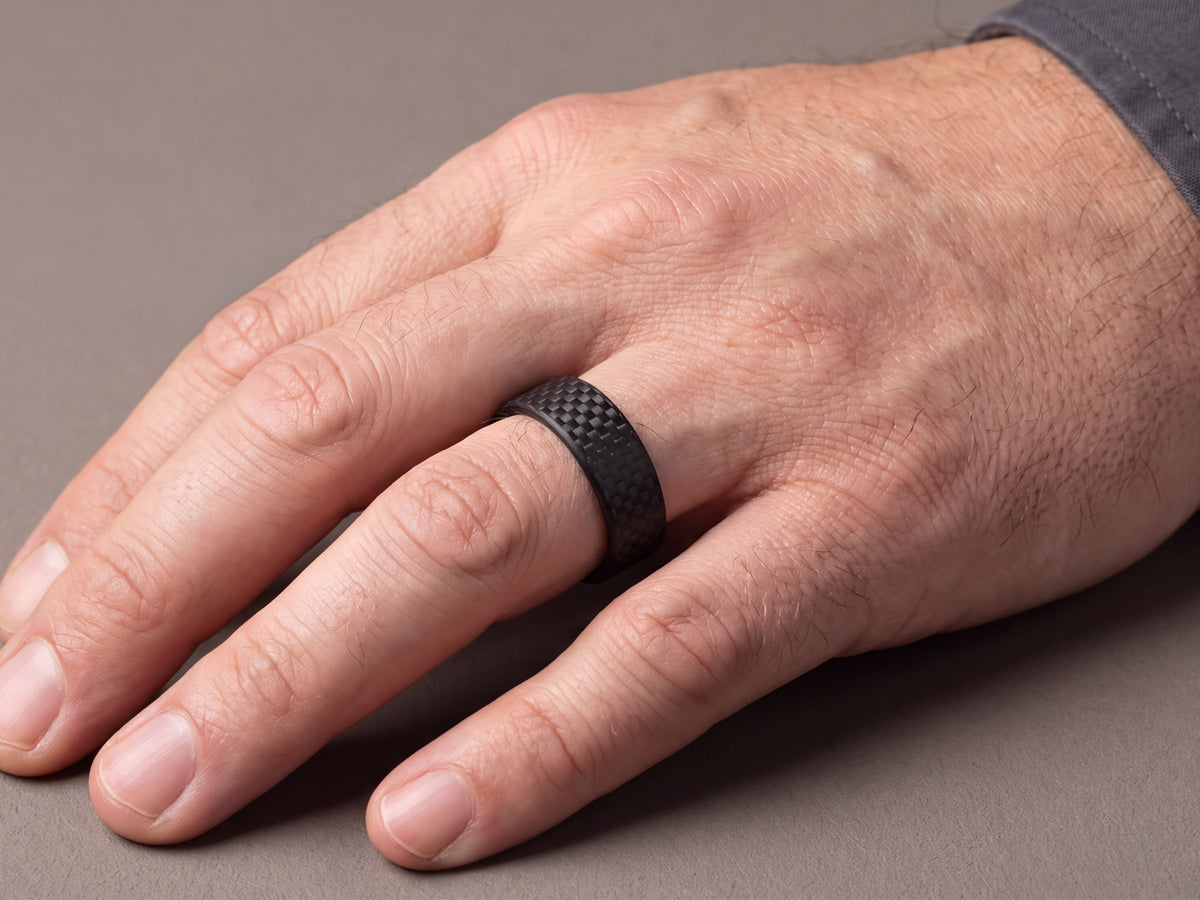 CarbonFG WeaveForce Gridlock 6mm carbon fiber ring worn on a left ring finger, hand at rest on a gray surface