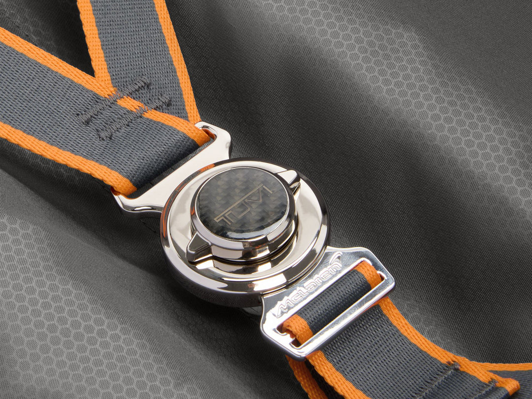 Close-up of McLaren harness-inspired compression straps with chrome hardware and Papaya orange accents