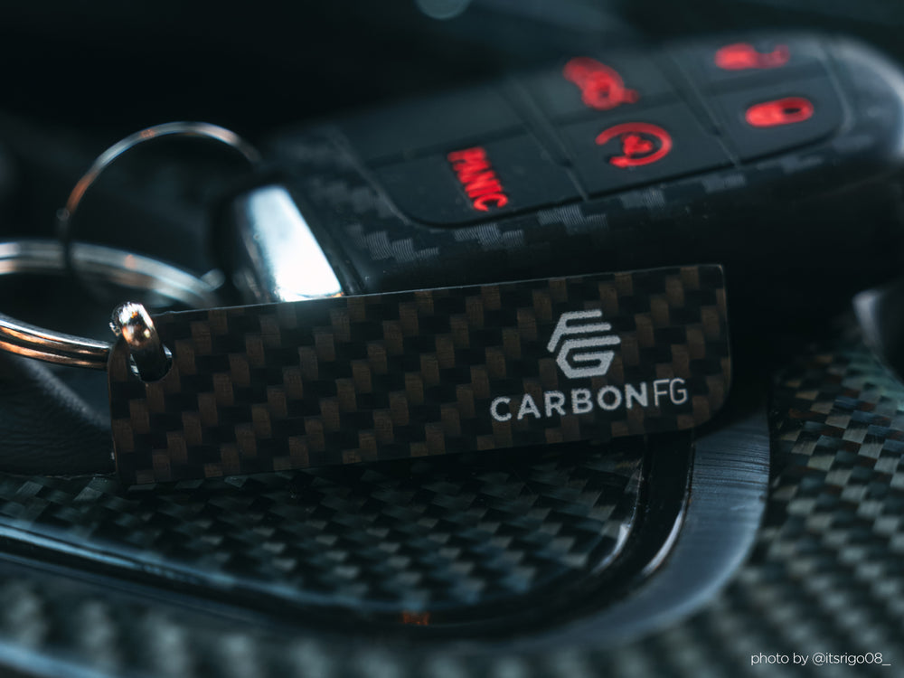 Close-up of a sleek solid carbon fiber key tag with matte 3K twill weave texture on a dark background