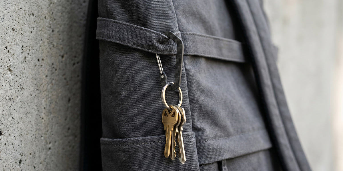 CarbonFG HexClip CF carbon fiber carabiner keychain clipped to grey canvas backpack strap with keys attached, 3K twill weave