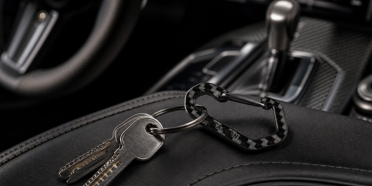 CarbonFG HexClip CF carbon fiber carabiner keychain with keys resting on black leather car seat, luxury vehicle interior with carbon fiber trim in background