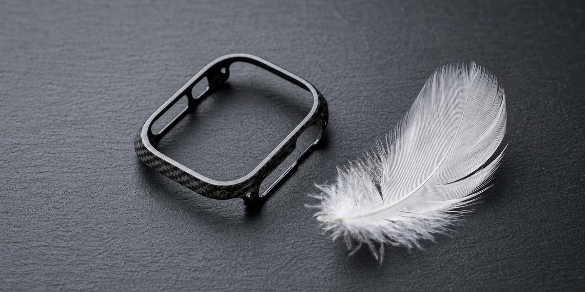 CarbonFG CarboShield carbon fiber Apple Watch Ultra case resting beside a white feather on dark slate surface, showing lightweight design