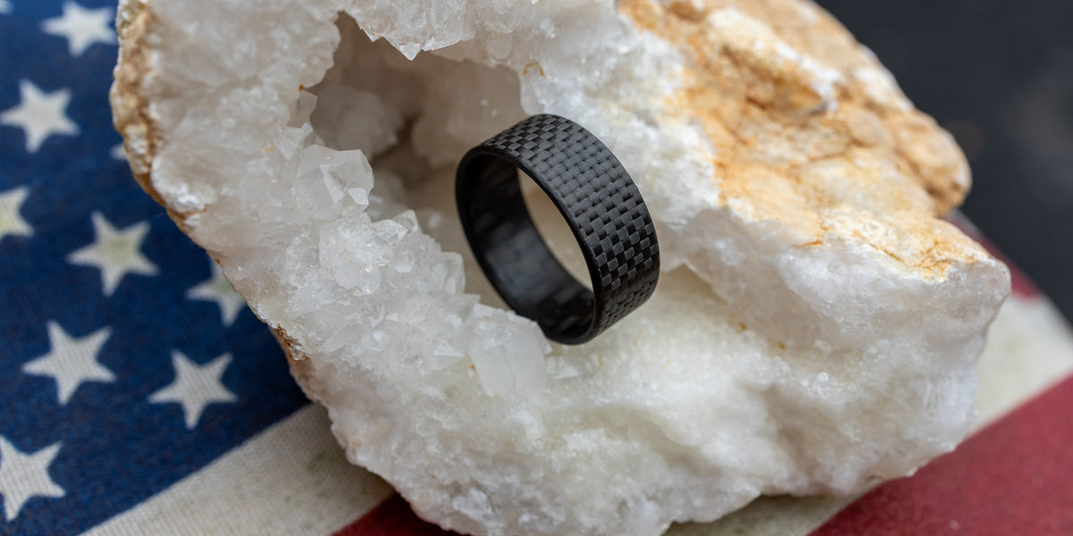 8mm Gridlock carbon fiber ring displayed inside a quartz crystal geode with an American flag backdrop, showcasing USA craftsmanship and material strength
