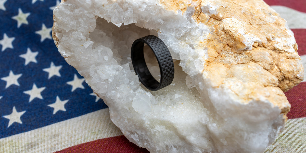 6mm Gridlock carbon fiber ring resting inside a white crystal geode with an American flag backdrop, symbolizing strength and patriotism.