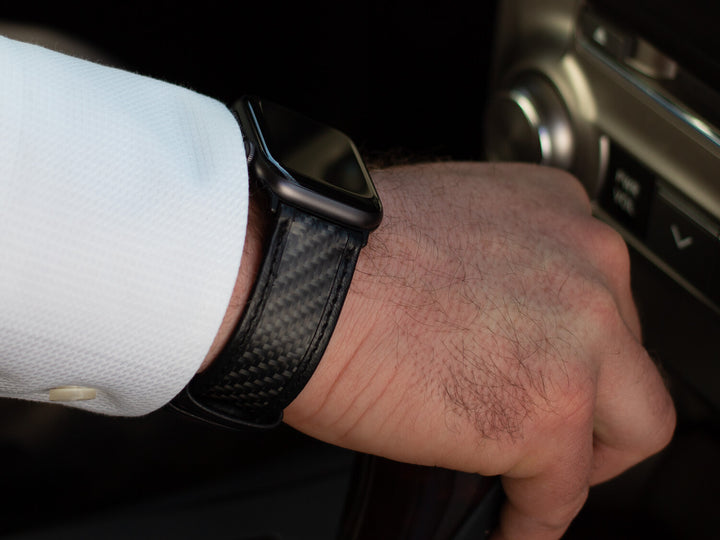 Close-up of an Apple Watch on a wrist, featuring the CarboBand carbon fiber and leather strap.