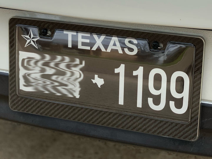 Mounted carbon fiber license plate frame on a vehicle with a clear cover, featuring a Texas license plate.