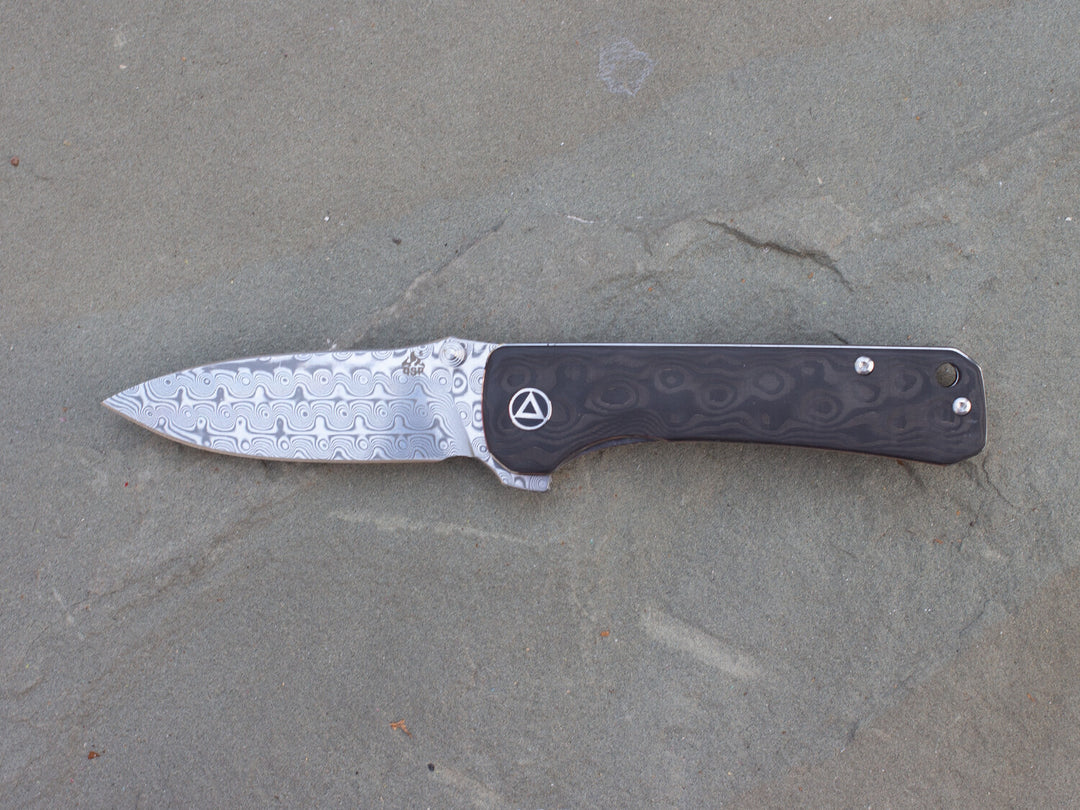 QSP Hawk Raindrop Carbon Fiber & Damascus Steel Liner Lock Knife on stone
